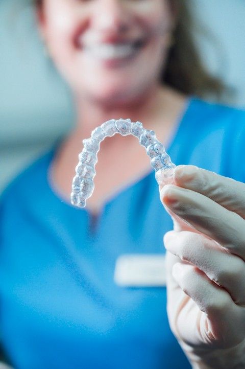 A clear Invisalign aligner held between two fingers